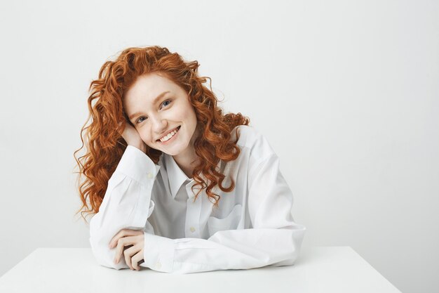 Linda mulher ruiva com cabelos cacheados, sorrindo, sentado à mesa.