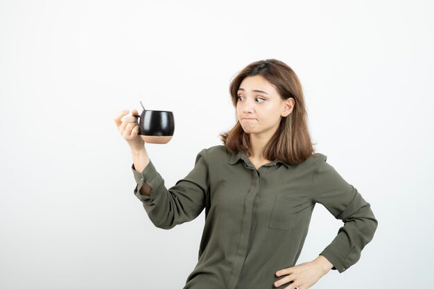 Linda mulher segurando a xícara de café e de pé sobre branco. Foto de alta qualidade