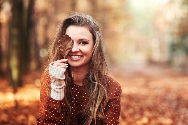 Linda mulher sorridente cobrindo os olhos com folhas outonais