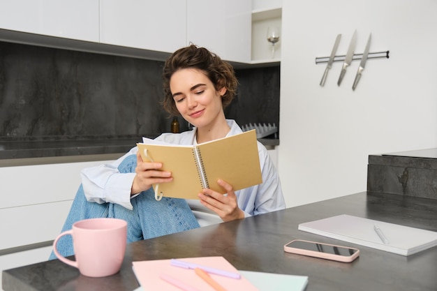 Linda mulher sorridente sentada com notebook na cozinha lendo notas estudando fazendo lição de casa