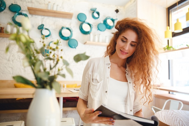 Linda ruiva sorridente jovem de pé na leitura de café