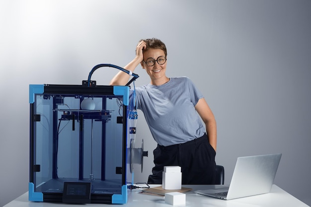 Foto grátis linda senhora caucasiana de óculos sorrindo perto da máquina de impressão 3d em seu escritório novas tecnologias para o conceito de pequenas empresas protótipos de computador na mesa tech ambiente jpg photo