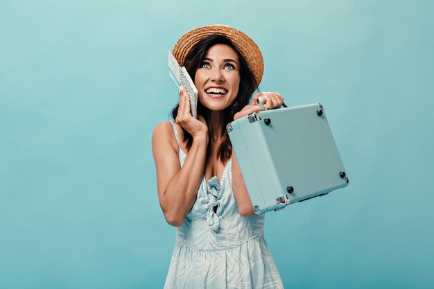 Linda senhora de vestido azul e chapéu está aproveitando as férias e segurando ingressos, mala