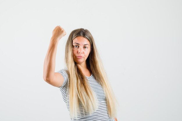 Linda senhora em t-shirt, mostrando o poder do braço e parecendo poderosa, vista frontal.