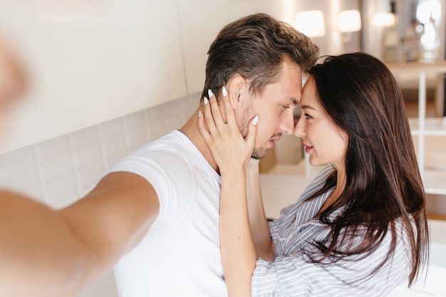 Linda senhora morena com manicure branca segurando o rosto do marido enquanto ele faz selfie