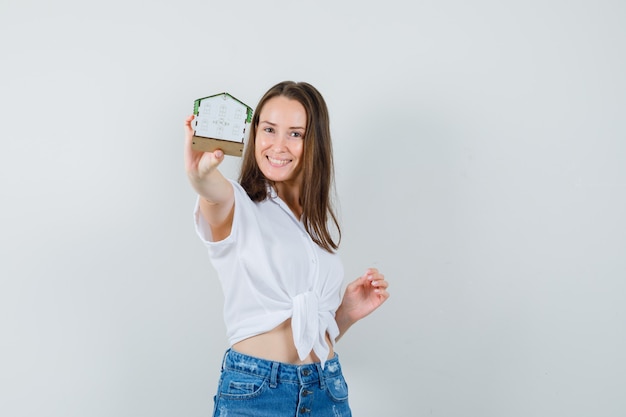 Foto grátis linda senhora mostrando a casa modelo em blusa branca e olhando feliz, vista frontal.