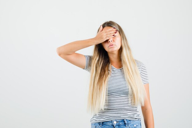 Linda senhora segurando a mão sobre os olhos em t-shirt e parecendo entediada, vista frontal.