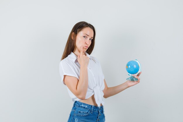 Linda senhora segurando o globo enquanto pensava em algo na blusa branca e olhando pensativa, vista frontal.