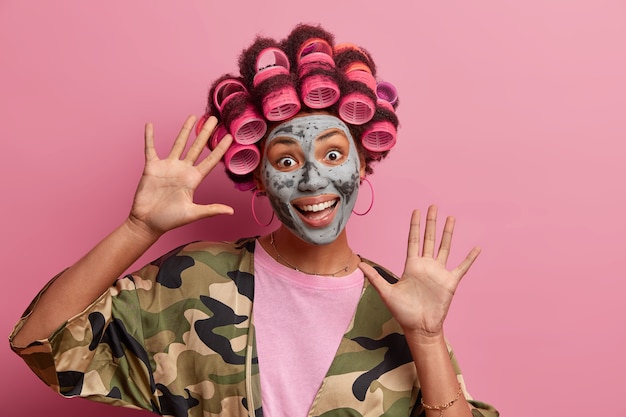 Linda senhora usando máscara para cuidados do rosto usando rolos de cabelo isolados