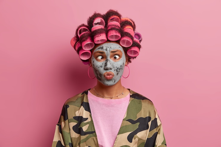 Foto grátis linda senhora usando máscara para cuidados do rosto usando rolos de cabelo isolados