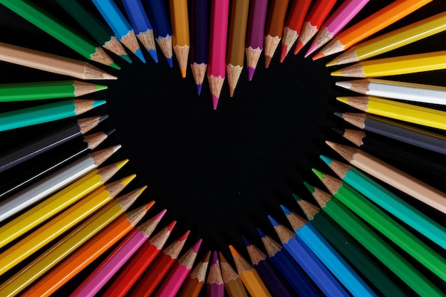 Linda vista de cima de um monte de lápis fazendo formato de coração com fundo preto
