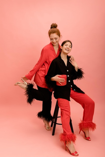 Lindas jovens irmãs caucasianas em trajes e sapatos idênticos se divertem no fundo rosa Conceito de juventude