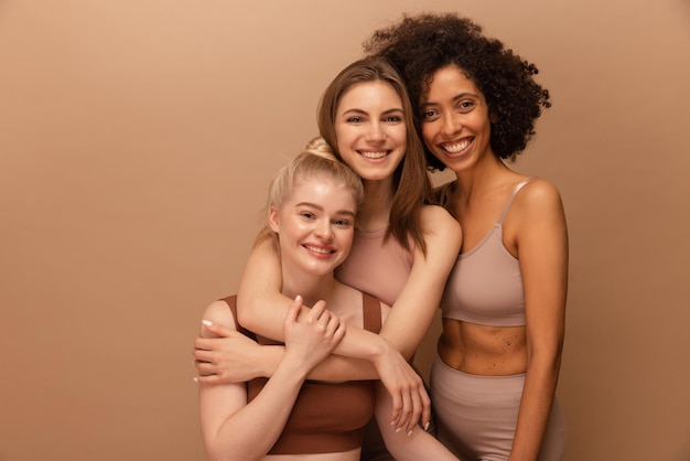 Lindas jovens mulheres caucasianas e africanas em lingerie posando em fundo bege Conceito de estilo de vida