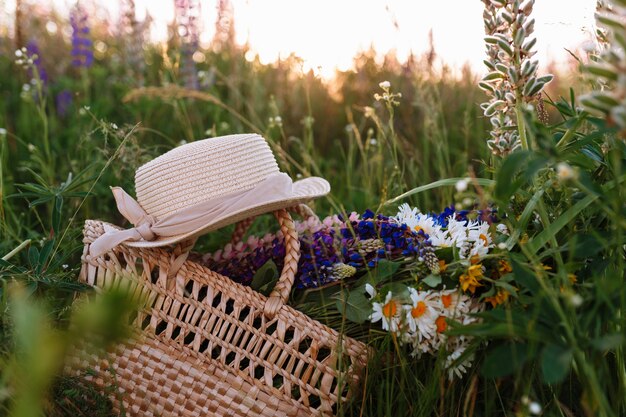 lindo buquê de tremoços encontra-se em um saco junto com um chapéu de palha na grama no campo.