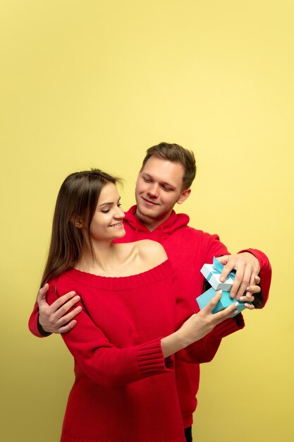 Lindo casal apaixonado abrindo presente na parede amarela do estúdio