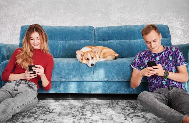 Lindo casal com celulares e fofo corgi no sofá