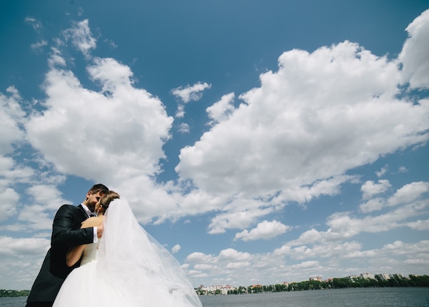 Lindo casal de noivos no fundo do céu azul, água