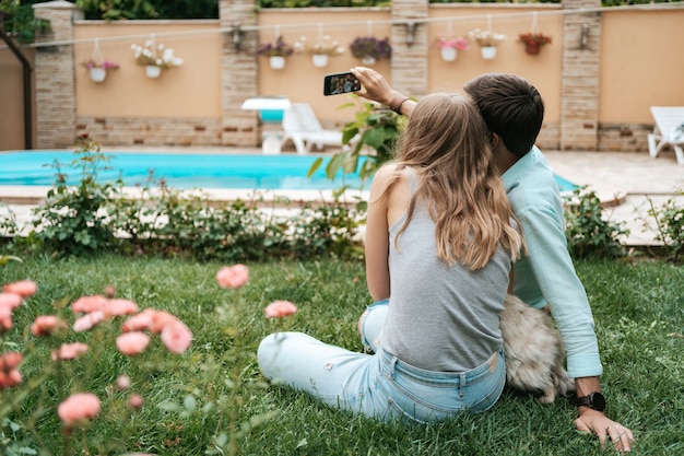 Lindo casal feliz fazendo selfie com seu adorável cachorro no quintal enquanto está sentado na grama