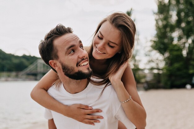 Lindo casal jovem está conversando e sorrindo enquanto caminha na praia em um dia ensolarado