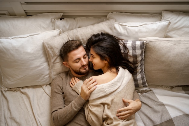 Lindo casal jovem relaxando na cama e sorrindo, se abraçando