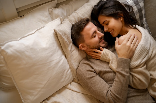 Lindo casal jovem relaxando na cama e sorrindo, se abraçando