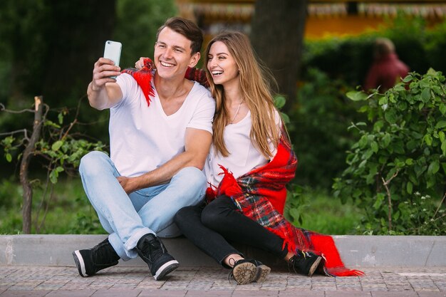 Lindo casal jovem relaxando no parque e fazendo selfie