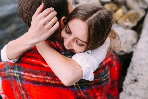 Foto grátis lindo casal jovem sentado em um aterro de pedra, enrolado em um cobertor