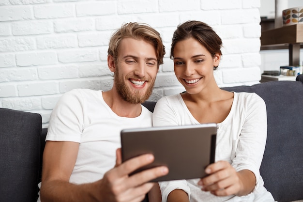 Lindo casal olhando tablet sorrindo sentado no sofá em casa.