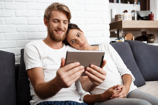 Lindo casal olhando tablet sorrindo sentado no sofá em casa.