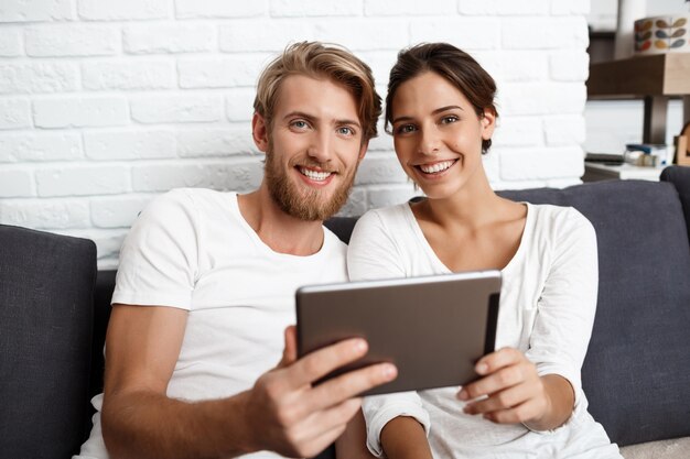 Lindo casal segurando a tablet sorrindo para casa.