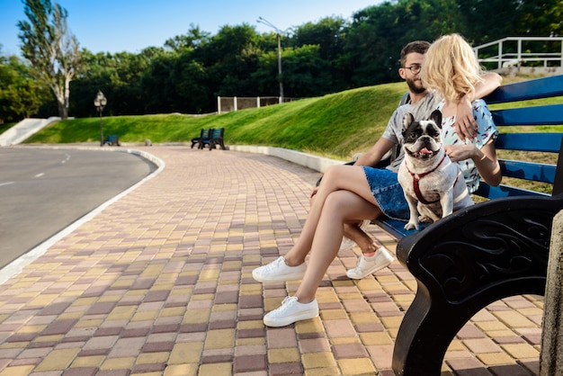 Lindo casal sentado com bulldog francês no banco do parque