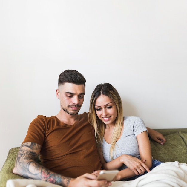 Foto grátis lindo casal sentado no sofá olhando para o telefone inteligente