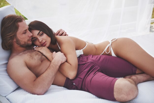 Lindo casal sexy rapaz e garota vestindo trajes de banho quando na praia. Romanticamente deitado na areia.