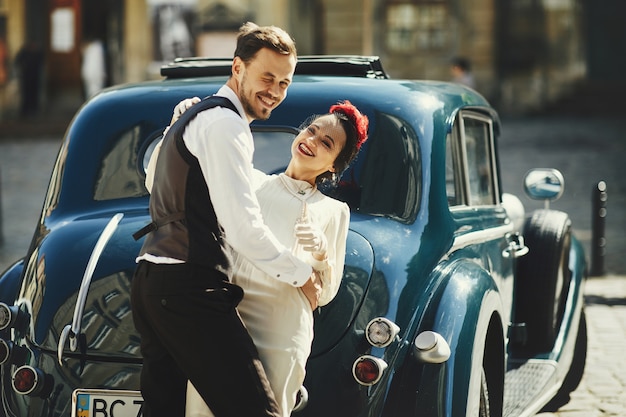 Lindo casal vestida em estilo anos 30 abraços na rua em pé diante de um carro velho