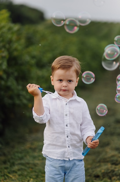 Lindo garoto brincando com bolhas em dia de sol no jardim.