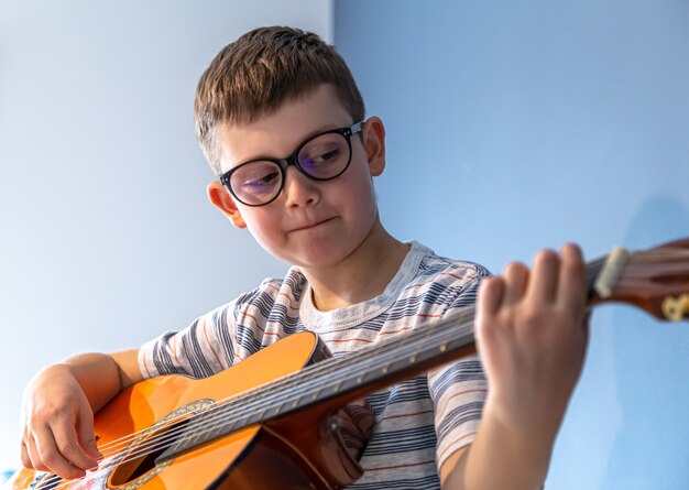 Lindo garoto de óculos aprende a tocar violão clássico em casa.