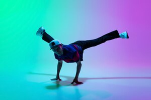 Lindo menino esportivo dançando hiphop em roupas elegantes em fundo gradiente colorido no salão de dança em luz neon
