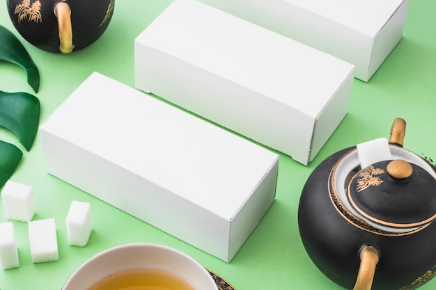Linha de caixas brancas com cubos de açúcar e chá de ervas em pano de fundo de papel verde