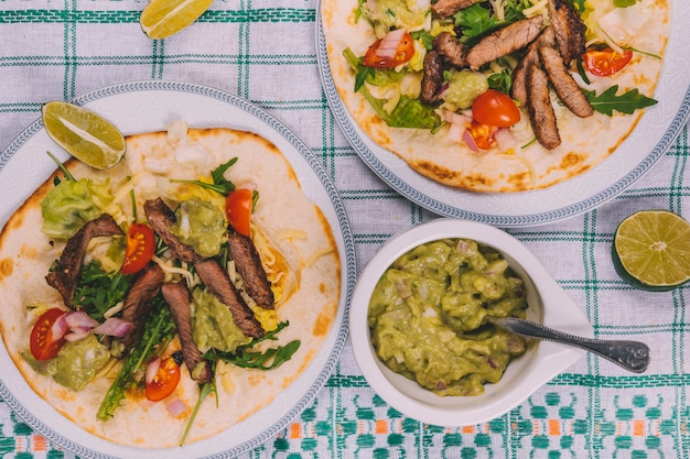 Foto grátis listras de carne mexicana com legumes em tortilla com guacamole sobre toalha de mesa