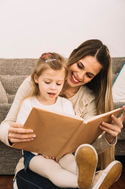 Livro de leitura mãe alegre para filha perto do sofá