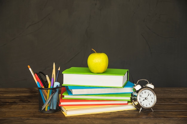 Foto grátis livros didáticos com copo de lápis e relógio na mesa