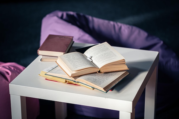 Livros em uma pequena mesa branca em um fundo desfocado do interior com pufes