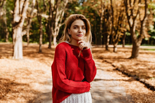 Loira deslumbrante em roupas elegantes, olhando longe na floresta de outono.