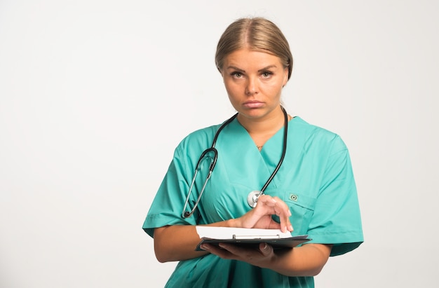 Loira médica de uniforme azul, segurando um livro de recibos.