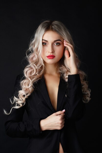 Loira sexy com cabelo longo encaracolado posa em jaqueta preta em um estúdio escuro