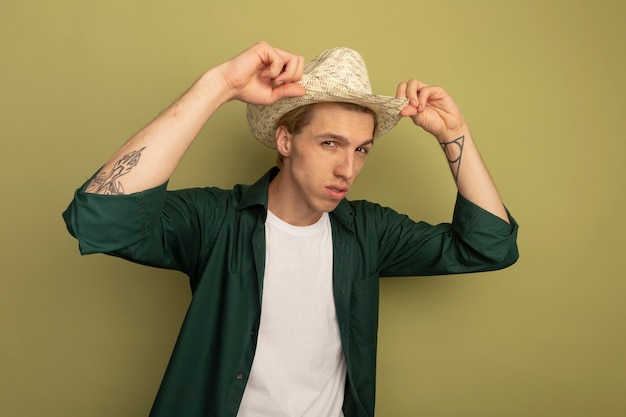 Foto grátis loiro confiante usando camiseta verde e chapéu segurando o chapéu