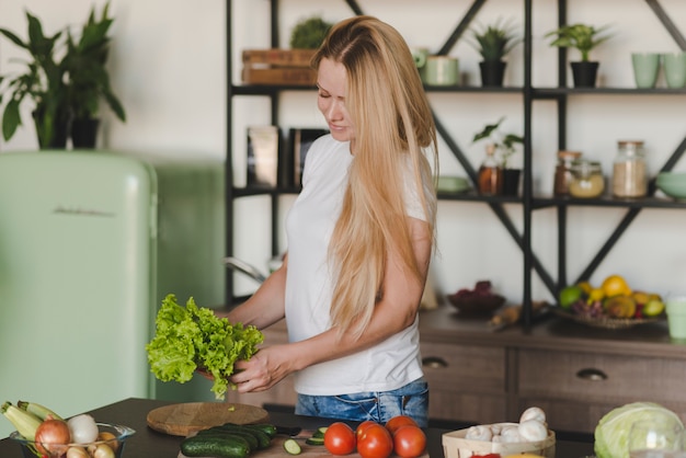 Foto grátis loiro, mulher jovem, ficar, em, cozinha, segurando, alface