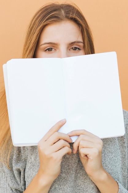 Loiro, mulher jovem, segurando, livro branco, sobre, dela, boca, contra, pêssego, fundo