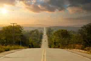 Foto grátis longa rodovia ladeada de árvores no interior com um céu colorido à tarde