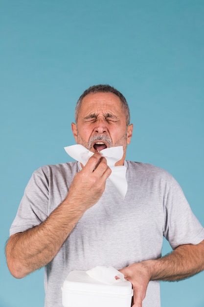 Último homem segurando o lenço de papel prestes a espirrar em fundo azul